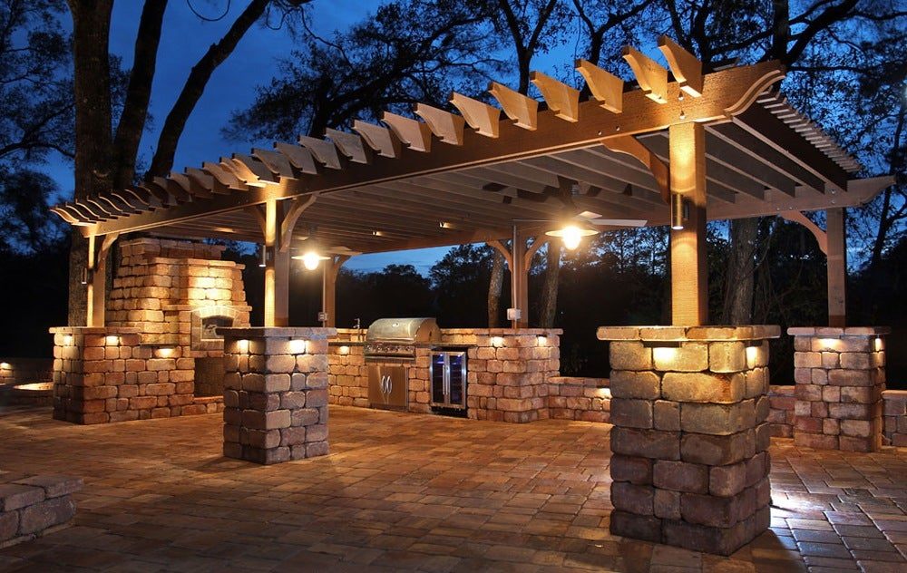 Outdoor kitchen and pergola with stone columns lit at night
